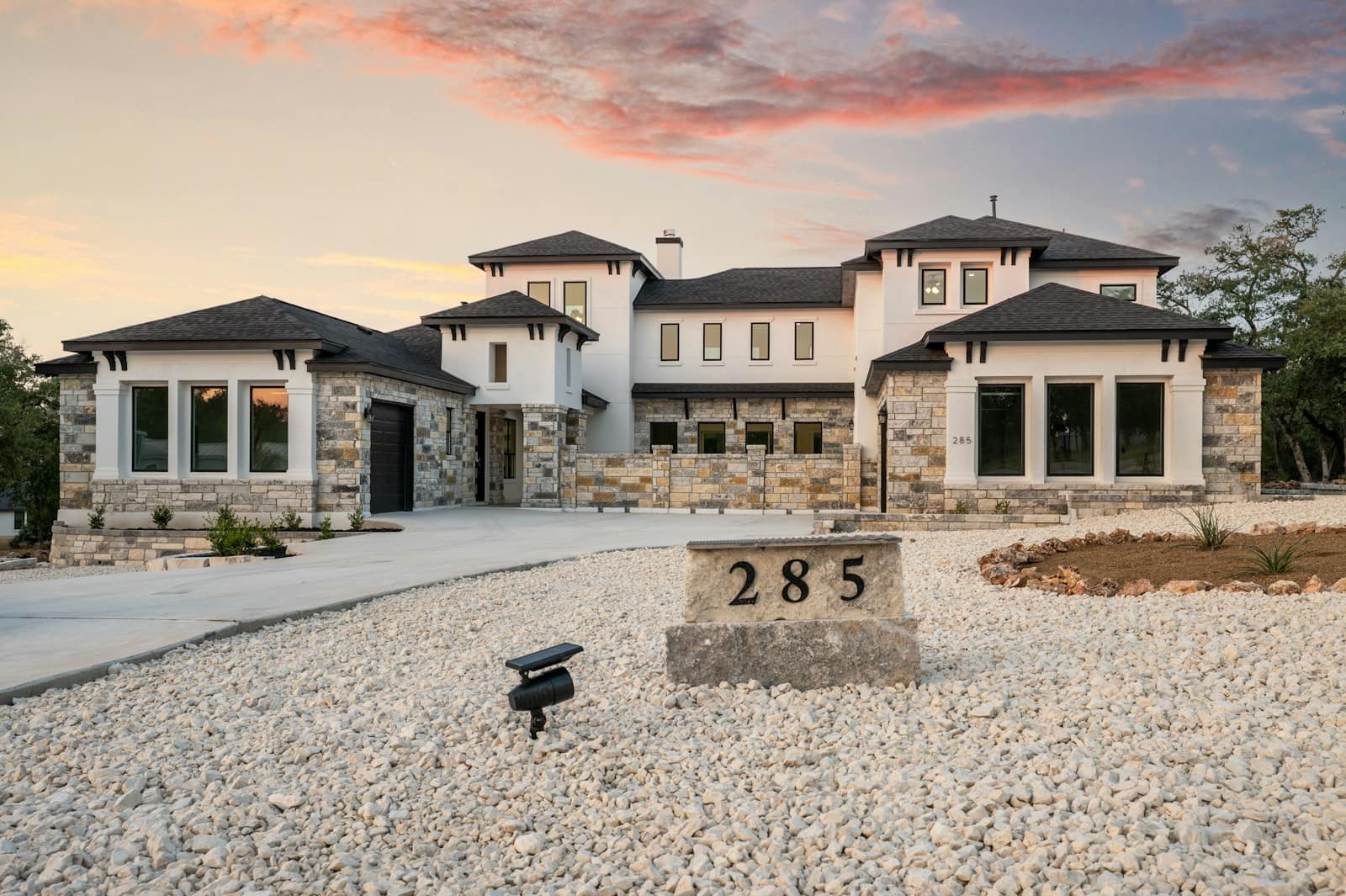 Modern stone-clad house at sunset, with the porch lights on